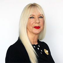 A photograph of a smiling lady with blonde hair wearing a black blouse and red lipstick.