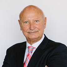 A headshot photo of a smiling older man wearing a suit what a peach and blue tie.