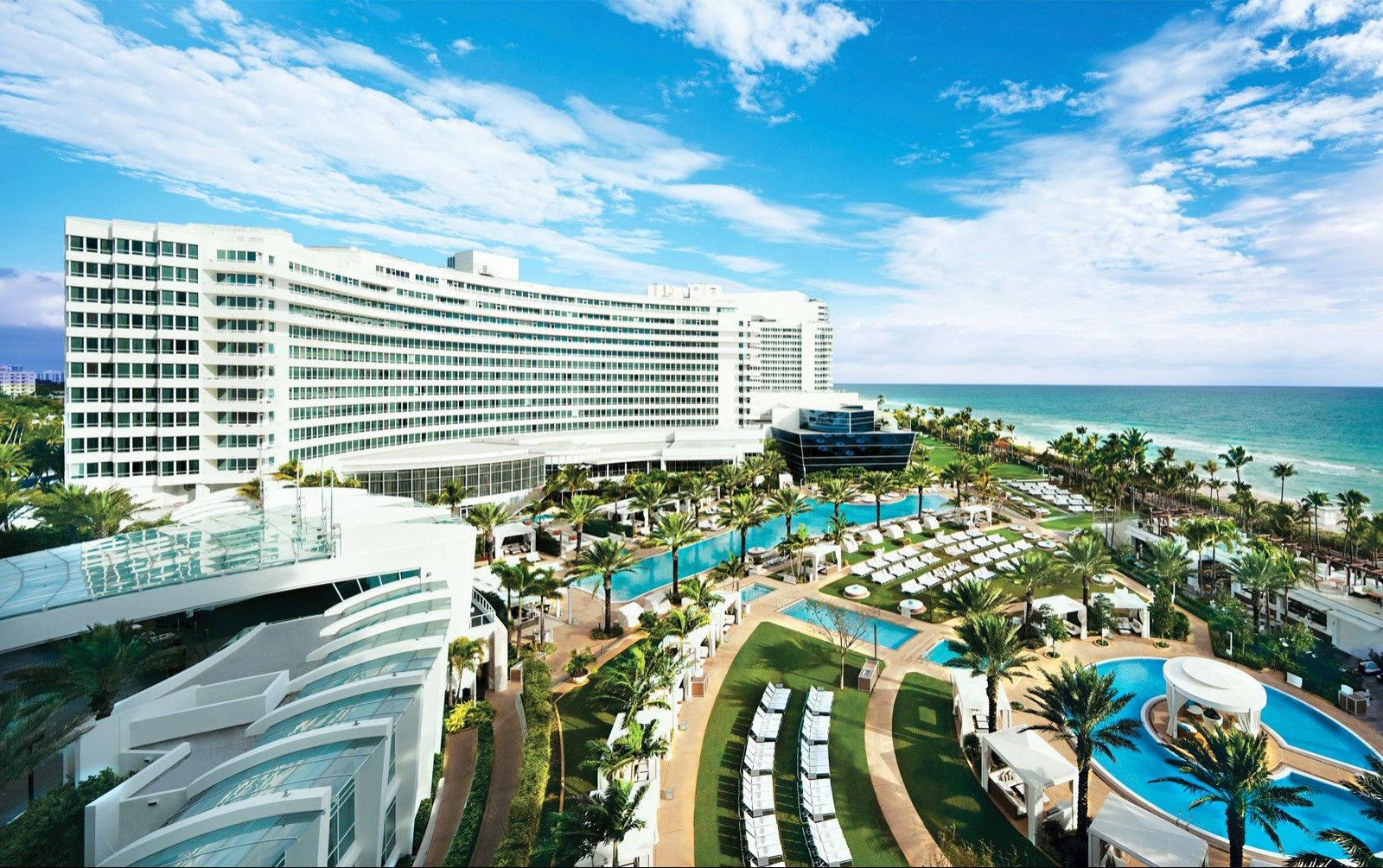 An aerial photograph of an outdoor pool and lounge area with palm trees and overseeing the beachfront.