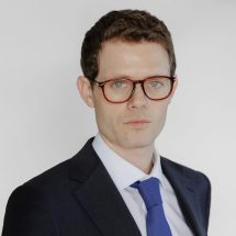 Man in a business suit wearing glasses and a blue tie.